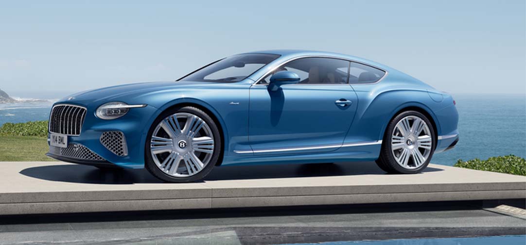 The Bentley Continental GT Azure in vibrant blue, showcased in profile view against an ocean backdrop, highlighting its elegant coupe silhouette and refined proportions.