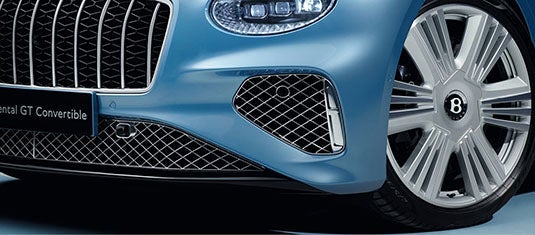 Close-up of the Bentley Continental GTC Azure’s front end, highlighting the polished alloy wheel, diamond-pattern grille, and detailed lower air intake mesh near the LED headlight.