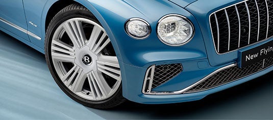 Close-up of the Bentley Flying Spur Azure’s front section, highlighting the signature grille, polished alloy wheel with the Bentley “B” center cap, and the Azure badge on the fender.