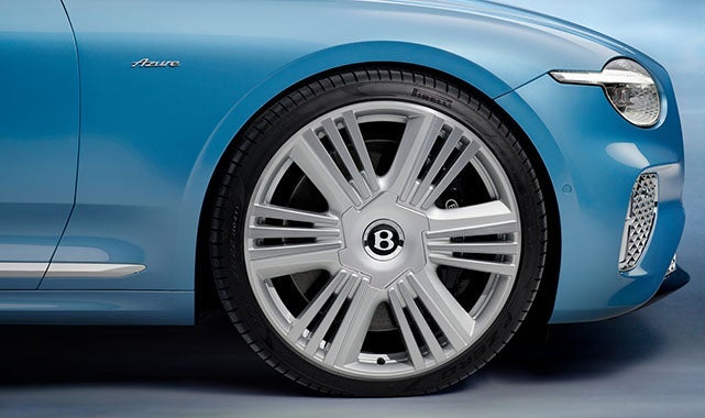 Side profile showing the large polished alloy wheel with a bold Bentley center cap and Azure fender badging on blue bodywork.