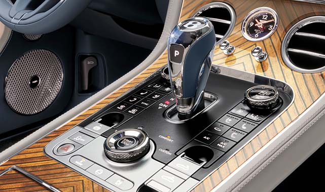 Premium center console featuring knurled control dials, a crystal-finished gear selector, and rich wood veneer with chrome accents.