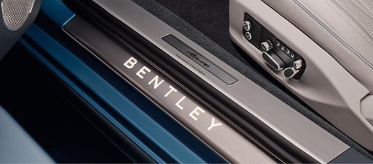 Close-up of the Bentley illuminated door sill plate with Azure branding, next to seat adjustment controls and diamond-stitched leather trim.
