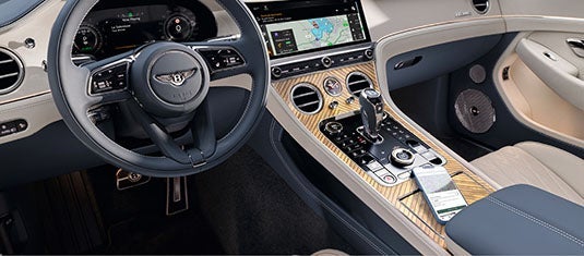Interior cabin shot of the Continental GTC Azure showing the infotainment screen, rotary dials, gear selector, and a smartphone resting on the wireless charging pad.