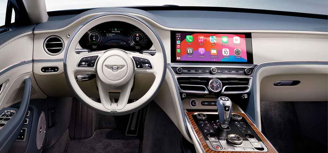 cockpit of the Bentley Flying Spur Azure featuring a two-tone steering wheel, full digital driver display, and wide infotainment screen with Apple CarPlay and rotary control interface.