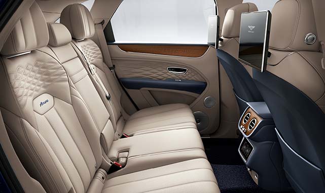Rear cabin of the Bentley Bentayga Azure, with quilted leather seats, wood trim, digital entertainment screens, and rear climate controls.