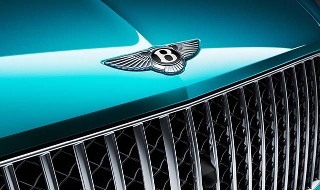 Close-up of the Bentley emblem on a turquoise hood with polished chrome grille detailing.