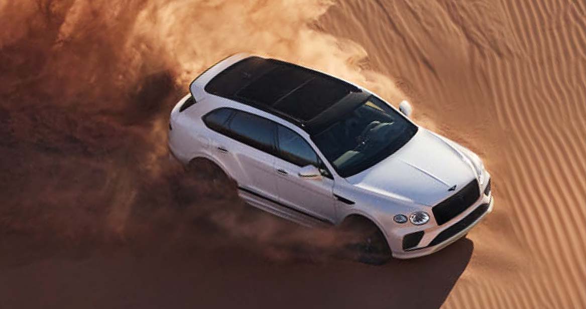 White Bentley Bentayga SUV kicking up sand while off-roading in the desert.