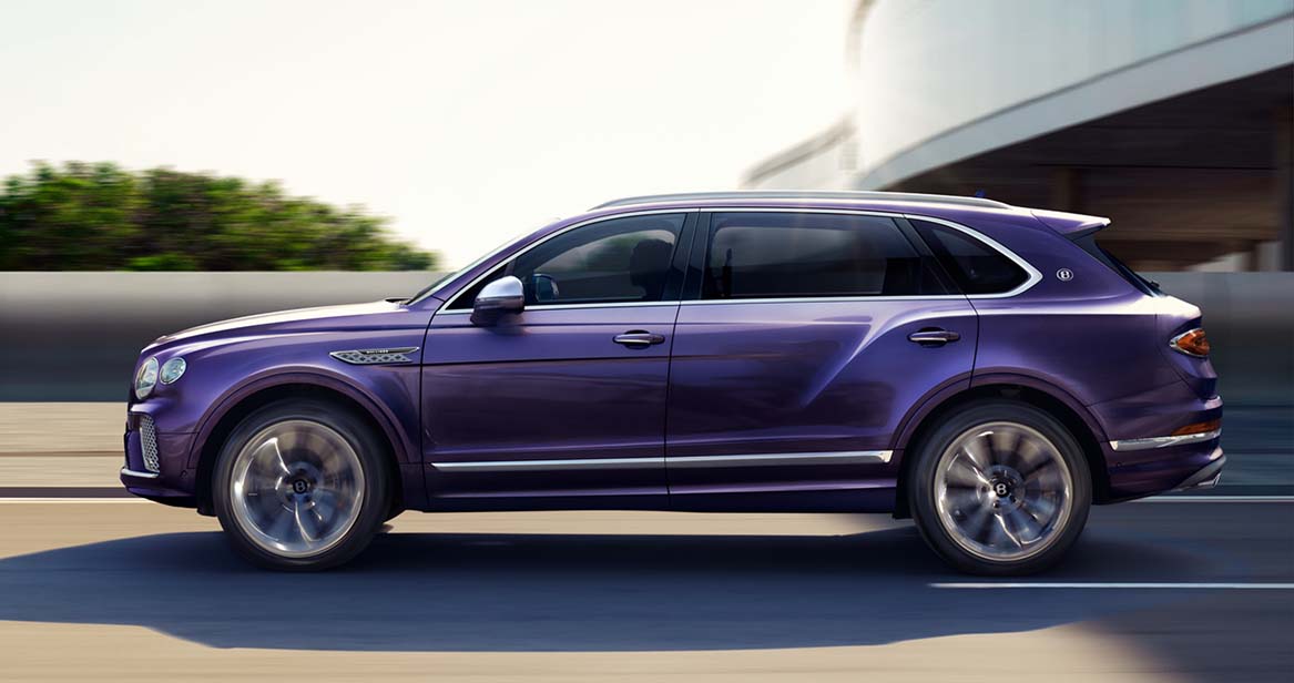 Purple Bentley Bentayga SUV driving at speed on a highway, showcasing performance and elegance.