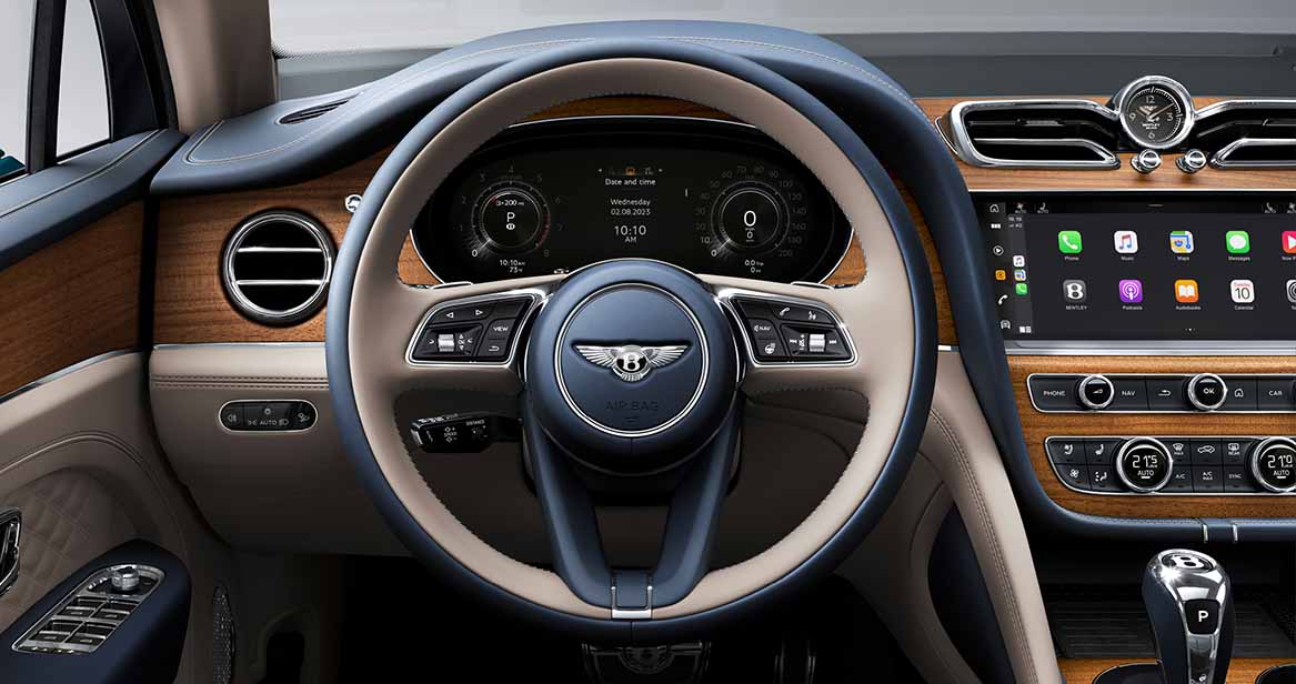 Bentley Bentayga steering wheel and dashboard showcasing luxurious wood trim, digital driver display, and infotainment system with Apple CarPlay.