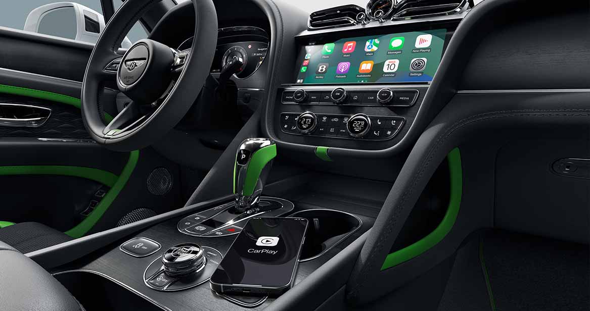 Bentley Bentayga interior with black leather and green accents, center console with gear selector, digital display, and Apple CarPlay interface.