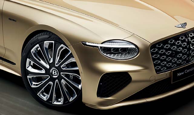 Close-up of the Bentley Continental GT’s front wheel, LED headlight, and grille, highlighting the intricate rim design and luxury details.