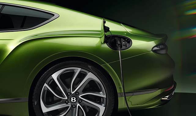 Rear three-quarter view of a green Bentley Continental GT plug-in hybrid with charging cable connected, emphasizing eco-performance and electrification.