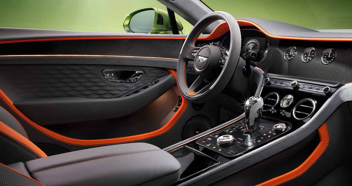 Modern black and orange interior of a Bentley Continental GT, with carbon fiber trim, stitched leather, and analog-style gauges on the dashboard.