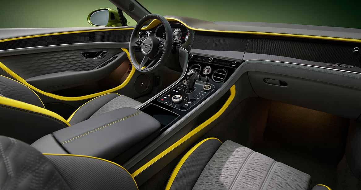 Interior view of the Bentley Continental GTC Speed showcasing a sporty design with carbon fiber trim, yellow accents, and a premium leather dashboard and seats.