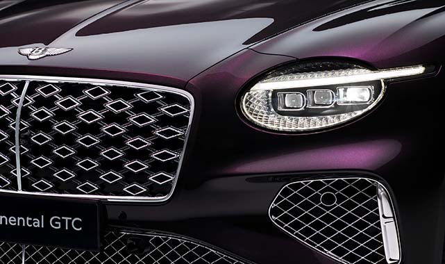Close-up of the front headlight and intricate diamond-pattern grille of a deep plum Bentley Continental GTC.