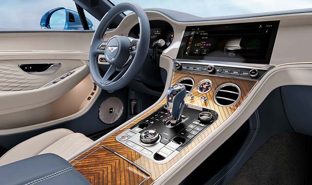 Front interior view of the Bentley Continental GTC featuring open-pore wood veneer, cream leather seats, and a center console with luxury controls.