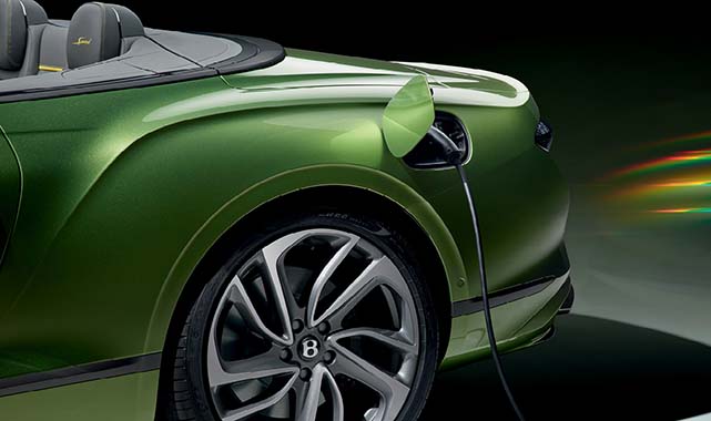 Rear quarter view of the Bentley Continental GTC in vibrant green with a charging cable plugged in, highlighting its hybrid capability.