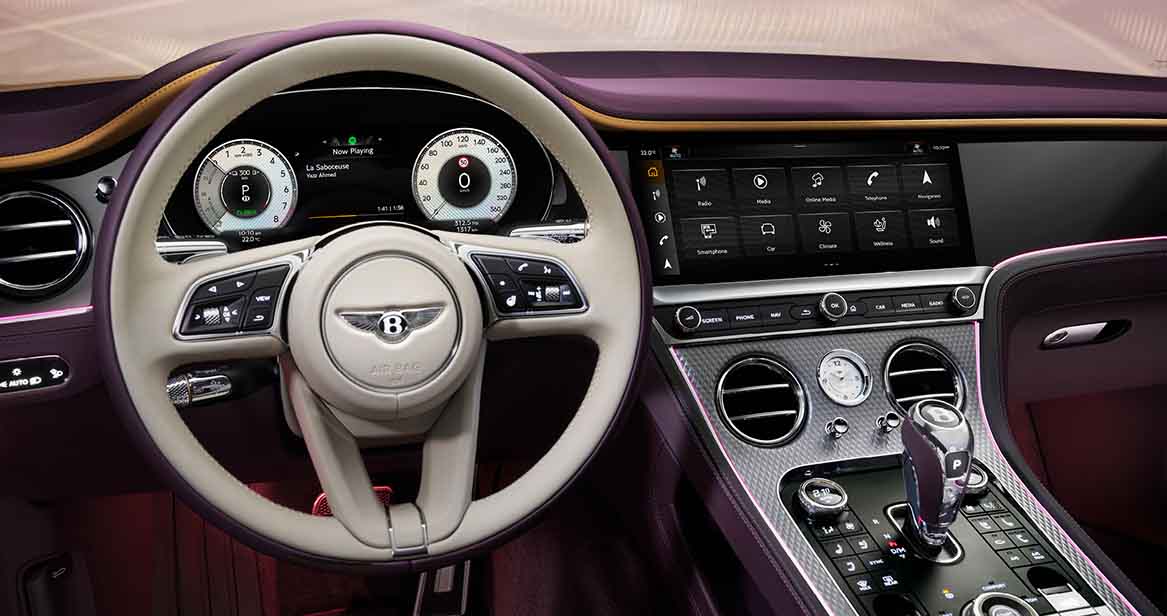 A luxurious Bentley interior featuring a two-tone leather steering wheel, fully digital instrument cluster, and large infotainment screen with chrome-accented center console.