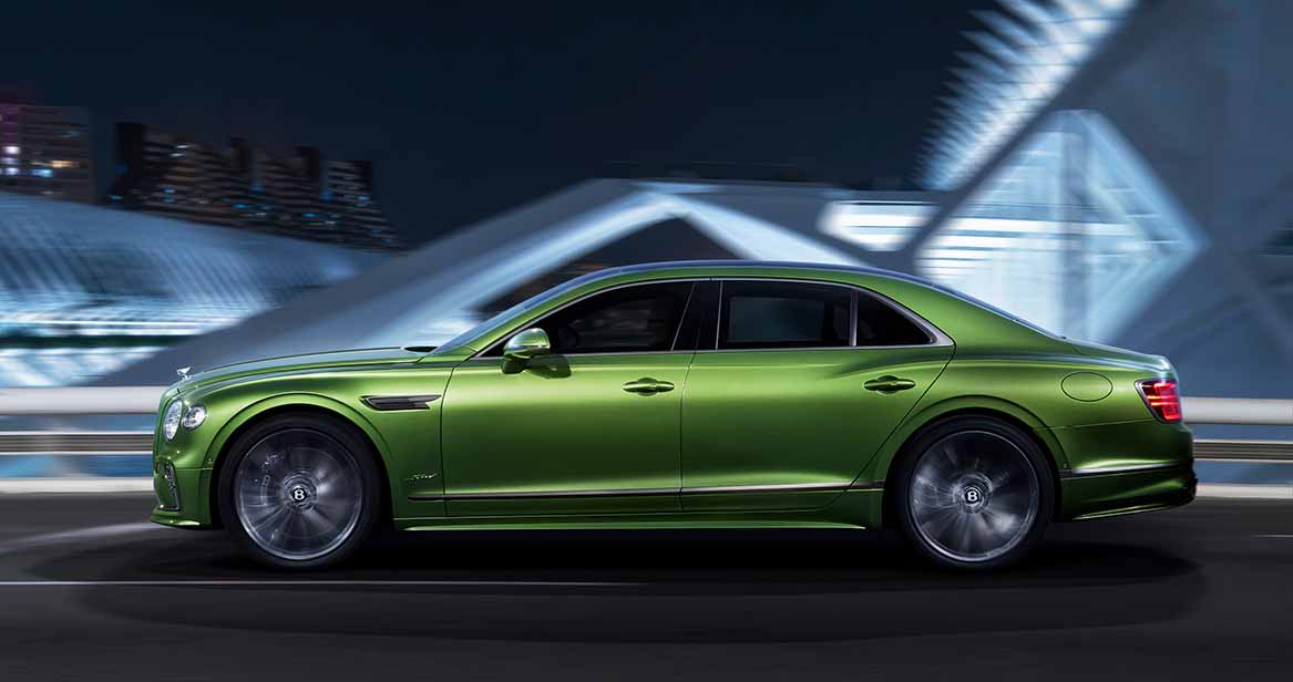 Side profile of the Bentley Flying Spur Speed in motion against a modern cityscape at night, showcasing luxury performance and aerodynamic design.