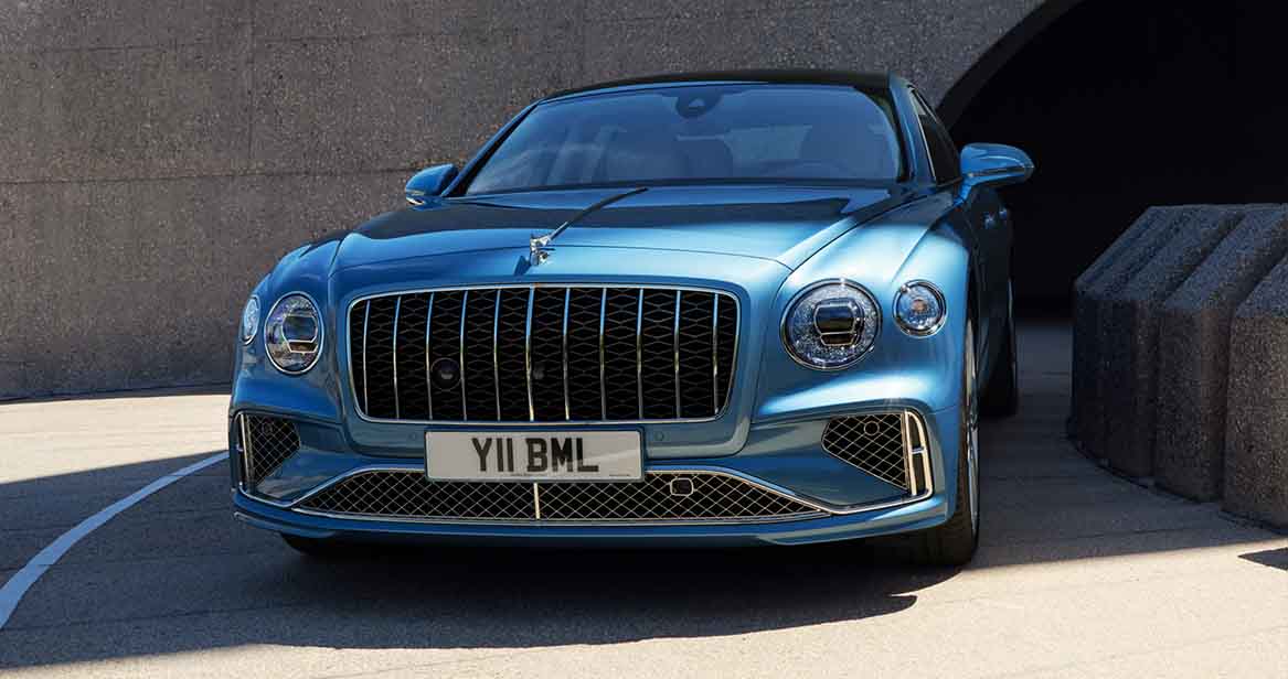 Front view of the Bentley Flying Spur Azure parked in sunlight, highlighting the bold matrix grille, iconic Flying B hood ornament, and signature headlamps.