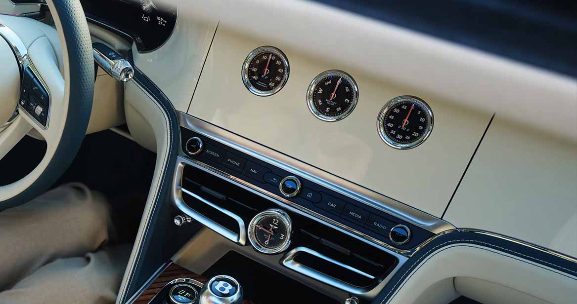 Close-up of Bentley’s dashboard analog dials for temperature, compass, and elevation set in cream leather with chrome detailing.