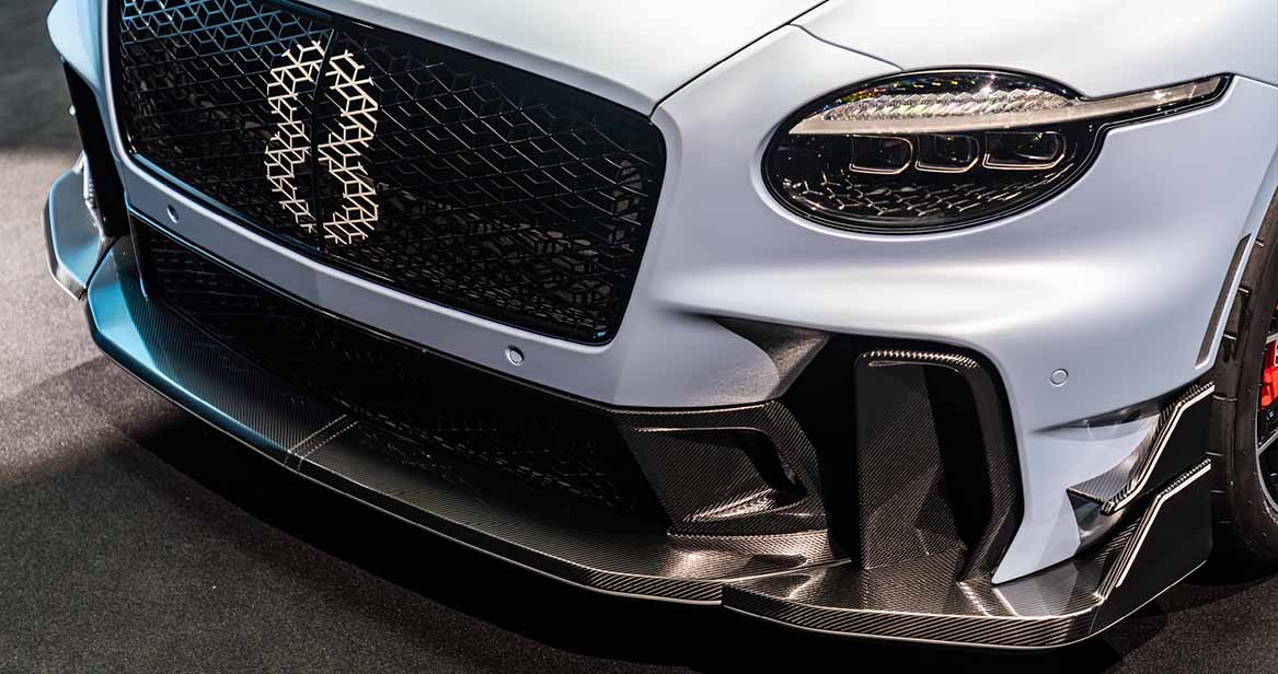Close-up of the 2026 Bentley Supersports front fascia featuring a carbon fiber splitter, honeycomb grille with illuminated Bentley B, and futuristic LED headlamps.