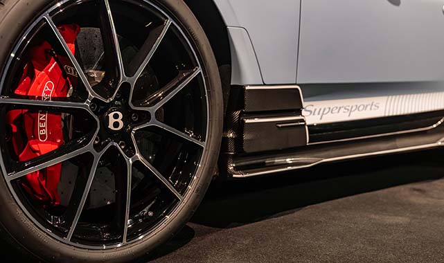 Close-up of 2026 Bentley Supersports 22-inch black alloy wheel, red Bentley brake caliper, and carbon fiber side skirt.