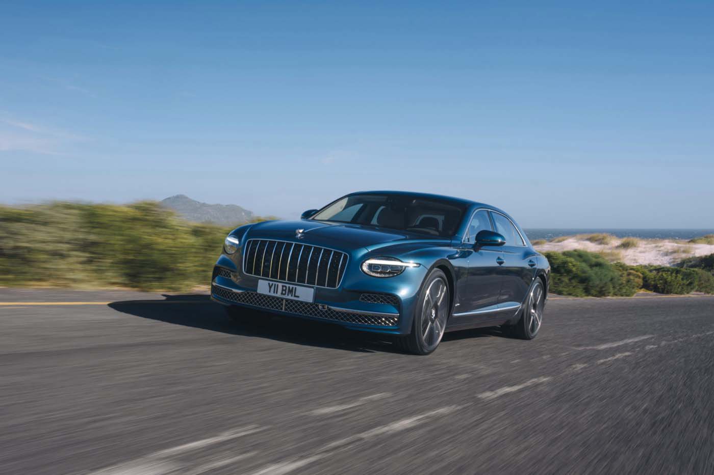 2027 Bentley Flying Spur Azure driving on a coastal road